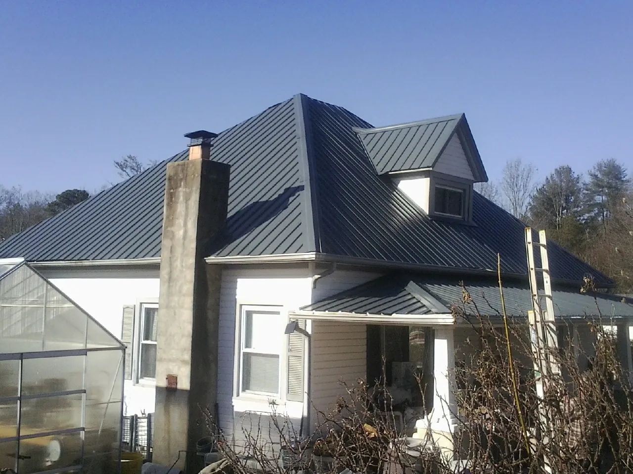 Dark blue standing seam metal roof on a white farmhouse with dormer — Slate & Tile Roof Repair by Roofing Brothers in Vienna