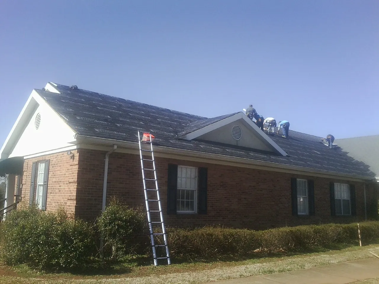 Crew tearing shingles off a brick ranch roof with a ladder set — Emergency Roof Repair work by our crew in Vienna